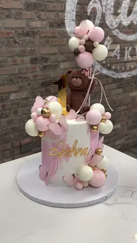 How sweet is this teddy bear first birthday cake for Asha? Soft pink and ivory, delicate butterflies, clusters of pastel balloons, and little touches of gold all come together around the cutest teddy bear holding her birthday balloons. We love the soft pink detailing and how every little element makes this cake feel extra special for her big ONE Text/Call the bakery for more info 201-391-6300 or email Sales@ALittleCake.com